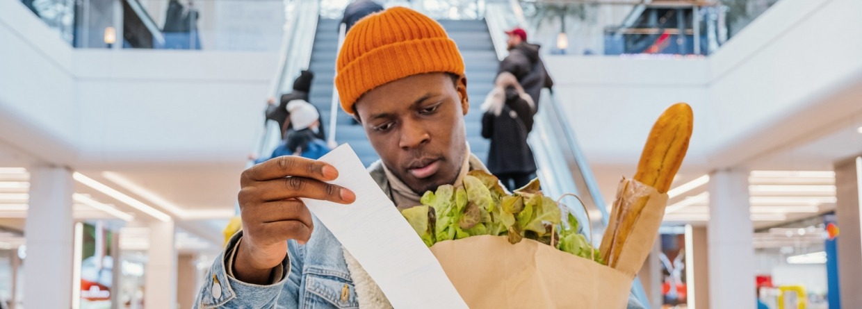 Een man heeft een zak met boodschappen vast en schrikt van de prijs